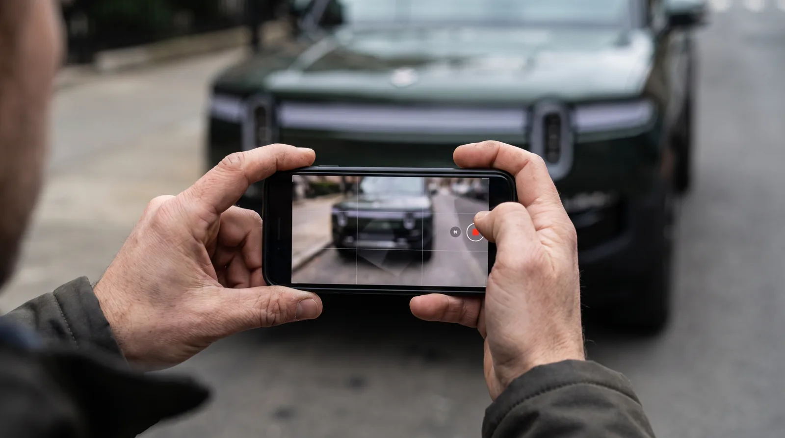 Hands holding a smartphone in landscape orientation framing the front of an SUV