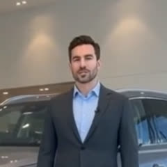 AI presenter in a dark suit standing in a car showroom